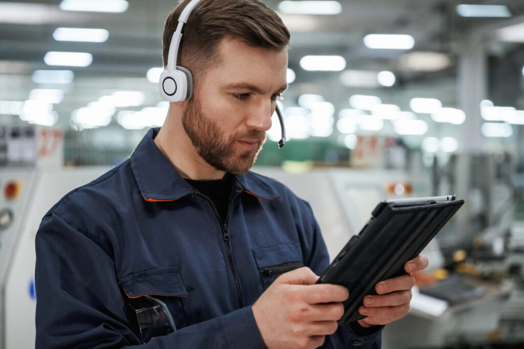 in headphones, with tablet. factory worker is indoors with hard hat